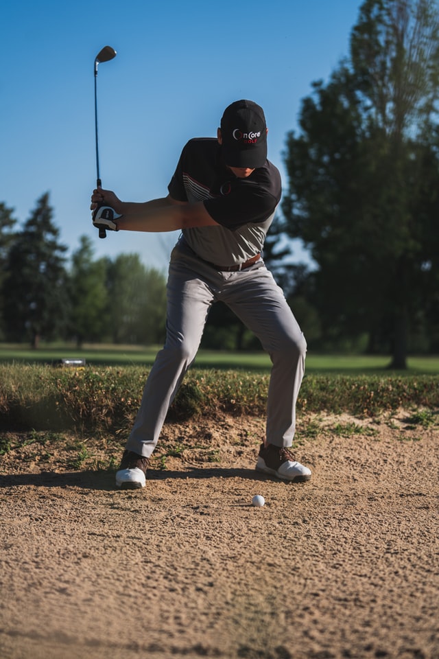 Male golfer in white shoes hitting a bunker shot